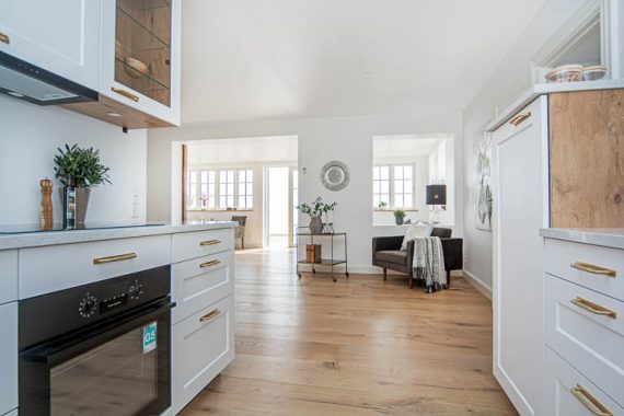 Fra køkkenet har man udsigten til vandet, set gennem stuerne. Med en professionel boligstyling får du en indretning, der fremhæver boligens kvaliteter og som samtidig er stylet til at give et flot og indbydende indtryk, der fanger købernes opmærksomhed.