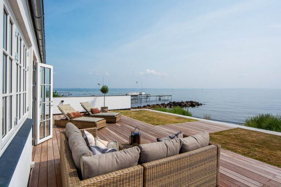 Unikke kvaliteter skal fremhæves og her gælder det en unik terrasse i vandkanten. Med denne boligstyling ville vi gerne synke ned i puderne nyde lyset og luften resten af dagen.